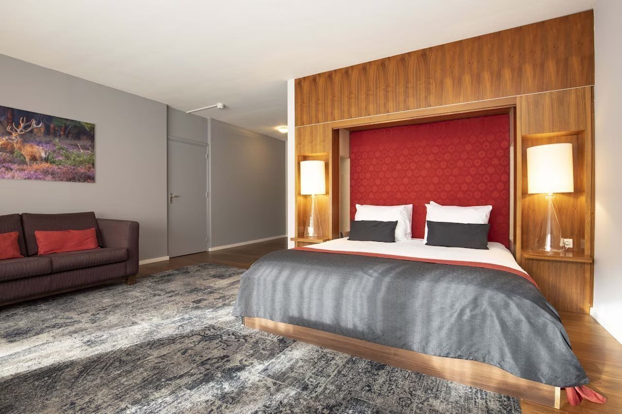 A modern hotel room with a large bed, a sofa, and a painting of a deer on the wall.