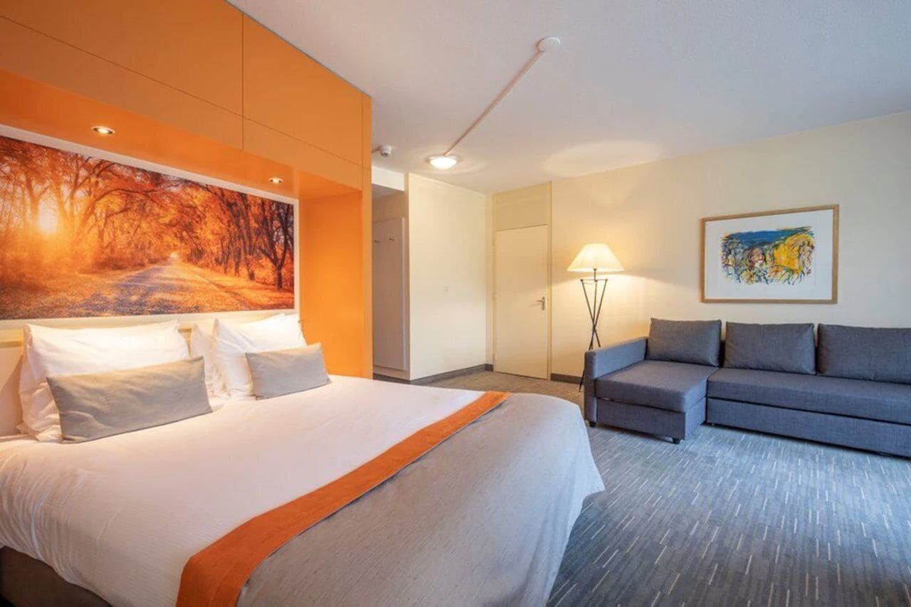 Una habitación de hotel con una cama grande, un sofá, un cuadro en la pared y una lámpara.