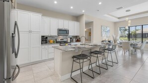Una cocina moderna con armarios blancos, un refrigerador de acero inoxidable, un microondas y una cafetera. Hay un comedor con una mesa y sillas.