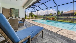 Un espacio exterior techado con piscina, sillones de descanso y un ventilador de techo.