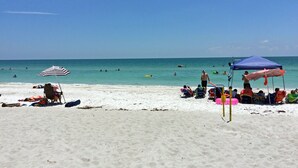 Una playa con gente tomando el sol y nadando, sombrillas y sillas de playa.