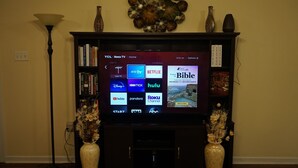 Ein Flachbildfernseher an der Wand über einem Kamin, der Symbole verschiedener Streaming-Dienste anzeigt.