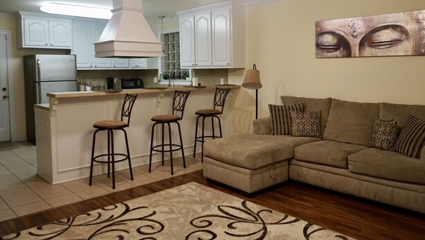 Eine moderne Küche mit weißen Schränken, einer integrierten Kücheninsel mit Barhocker, einem beigen Sofa und einem gemusterten Teppich.