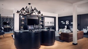 A modern interior with a central black reception desk, a large wall-mounted TV, and a seating area with white chairs and a brown sofa. - Gr8 Hotel Sevenum (Sevenum)