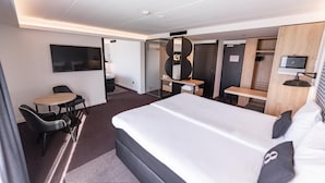 A modern hotel room with a large bed, a desk, a chair, a TV, and a wardrobe. - Gr8 Hotel Sevenum (Sevenum)