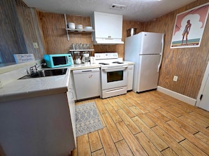 A compact kitchen with white appliances, a wooden floor, and a poster on the wall. - Heart of Ocean Drive - half block to the beach, 2 blocks to Main Street (North Myrtle Beach)
