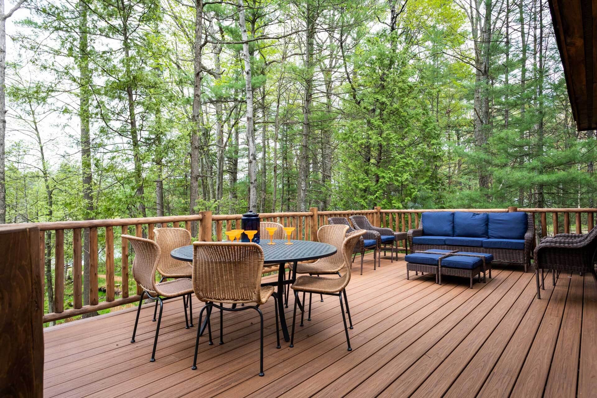Een houten terras met rieten meubels, een ronde tafel en een blauwe bank.