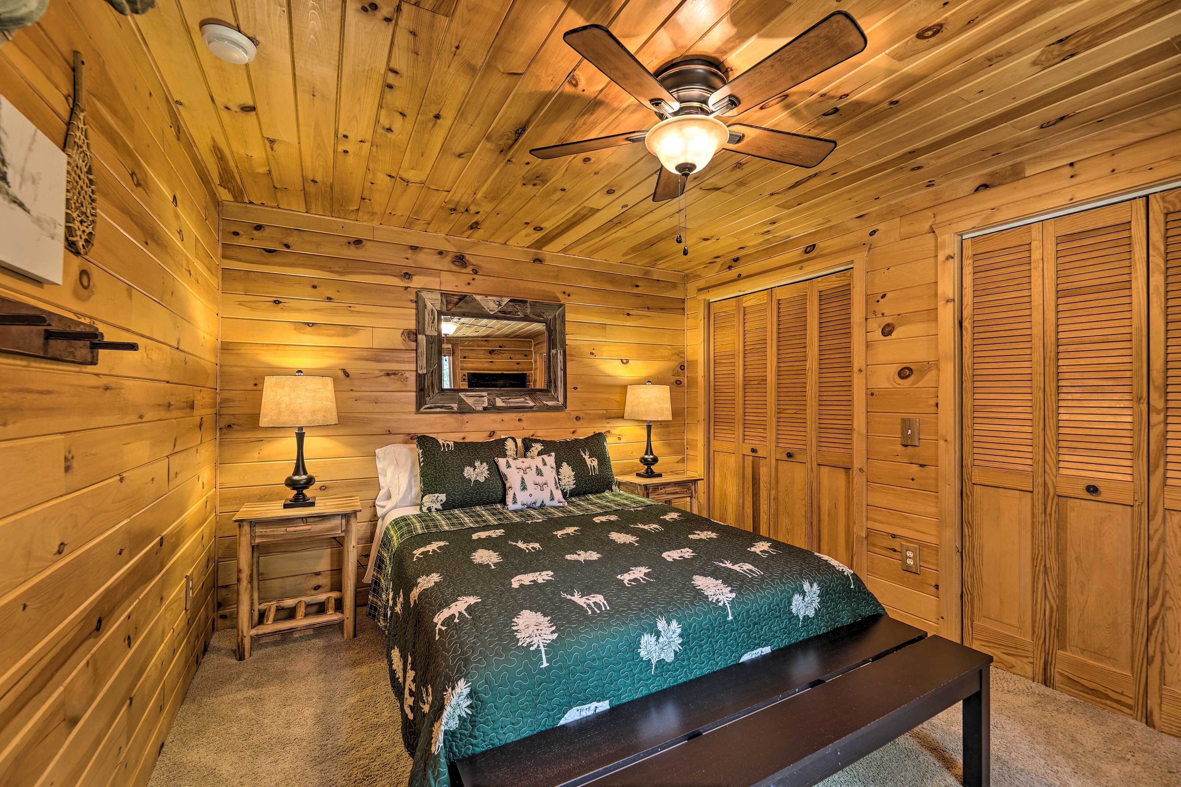 A wooden cabin bedroom with a bed, two bedside lamps, a ceiling fan, a mirror, and wooden closets.