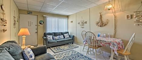 A living room with a sofa, a dining table with chairs, a patterned rug, and a ceiling with a grid pattern.