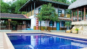 Una piscina con solárium de baldosas, un edificio con techo de paja y un muro de piedra con rocas.