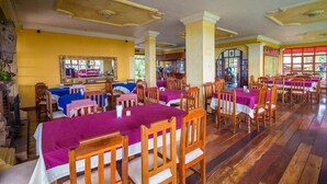 Un comedor con mesas y sillas de madera, paredes amarillas y un espejo grande.