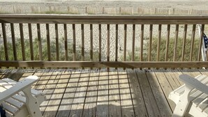 Eine Holzterrasse mit zwei weißen Stühlen mit Blick auf einen Sandstrand und den Ozean.