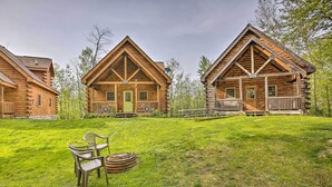 A log cabin with a porch and a dining area with chairs and a table. - Resort Cabin w/ Fire Pit: Golf, Hike and Play! (Rothbury)