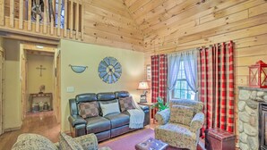 A cozy log cabin interior with a leather sofa, patterned armchairs, a stone fireplace, and a wooden ceiling. - Resort Cabin w/ Fire Pit: Golf, Hike and Play! (Rothbury)