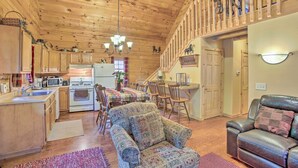 A cozy cabin interior with wooden floors, a dining area, a kitchen with modern appliances, and a comfortable seating area. - Resort Cabin w/ Fire Pit: Golf, Hike and Play! (Rothbury)