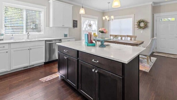 A kitchen with white cabinets, a dark island, pendant lights, and a window with blinds. - Family home downtown CDA walk to lake and dining (Coeur d'Alene)