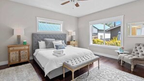 A bedroom with a large bed, a ceiling fan, a window with a view, a nightstand, and a chair. - Family home downtown CDA walk to lake and dining (Coeur d'Alene)