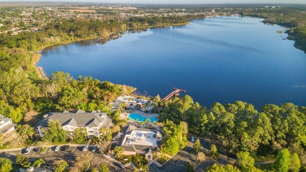 An aerial view of a lakeside resort with a swimming pool, a castle-like structure, and surrounding residential areas.