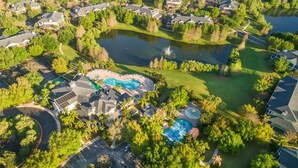 An aerial view of a residential area with multiple houses, a large pond, and two swimming pools.