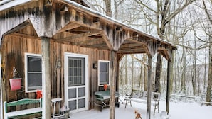 Eine rustikale Holzhütte mit Veranda, einer Bank, einem Tisch und einem Hund.