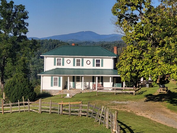 A two-story house with a green roof, a porch with chairs, and a wooden fence.
