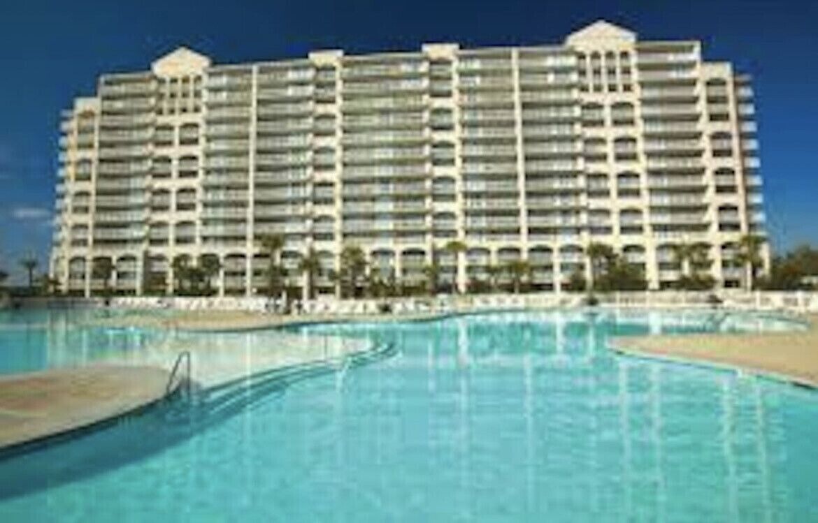 A large hotel with multiple balconies and a swimming pool in the foreground.