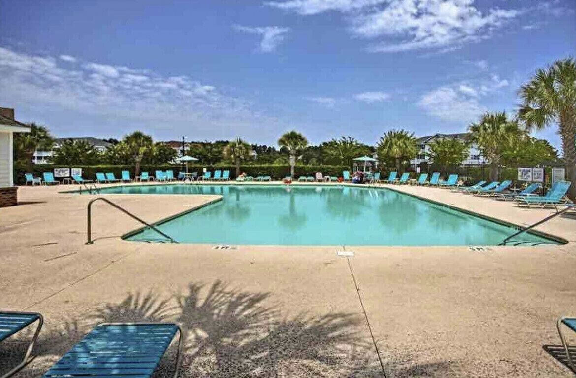 Une piscine rectangulaire avec une terrasse carrelée, entourée de chaises longues bleues et de palmiers.