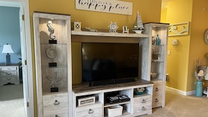 A living room with a wooden entertainment center, a flat-screen TV, and a sign above stating "THIS IS YOUR happy place".