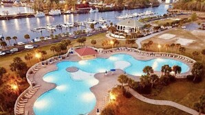 An aerial view of a resort with multiple swimming pools, a marina with boats, and a gazebo.