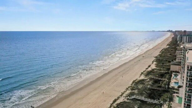 A beach with a clear view of the ocean and a row of buildings along the shore.