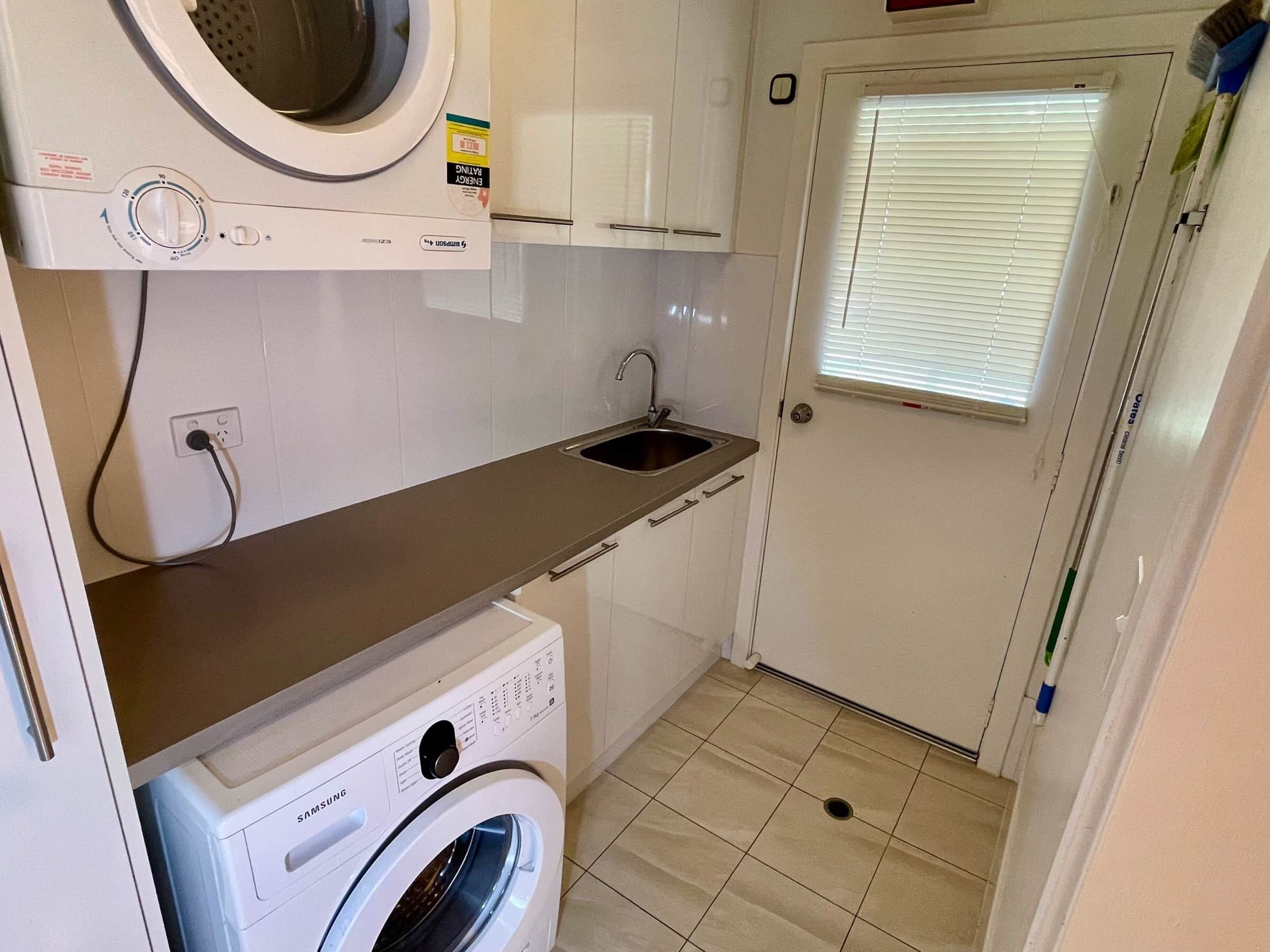 A compact laundry room with a washing machine, a dryer, a sink, and a door with a window.
