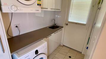 A compact laundry room with a washing machine, a dryer, a sink, and a door with a window.
