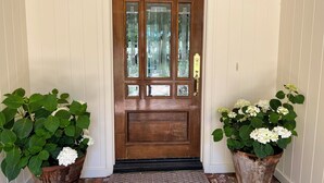 Una puerta de madera con paneles de vidrio y un picaporte de latón, flanqueada por dos grandes macetas con flores blancas.