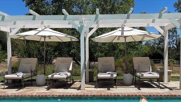 Zona de piscina con sillones reclinables y sombrillas, rodeada por una pérgola.