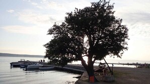 A waterfront area with a large tree, boats docked, and people relaxing by the water. - Holiday home mit Klimaanlage und Terrasse (Starigrad-Paklenica)