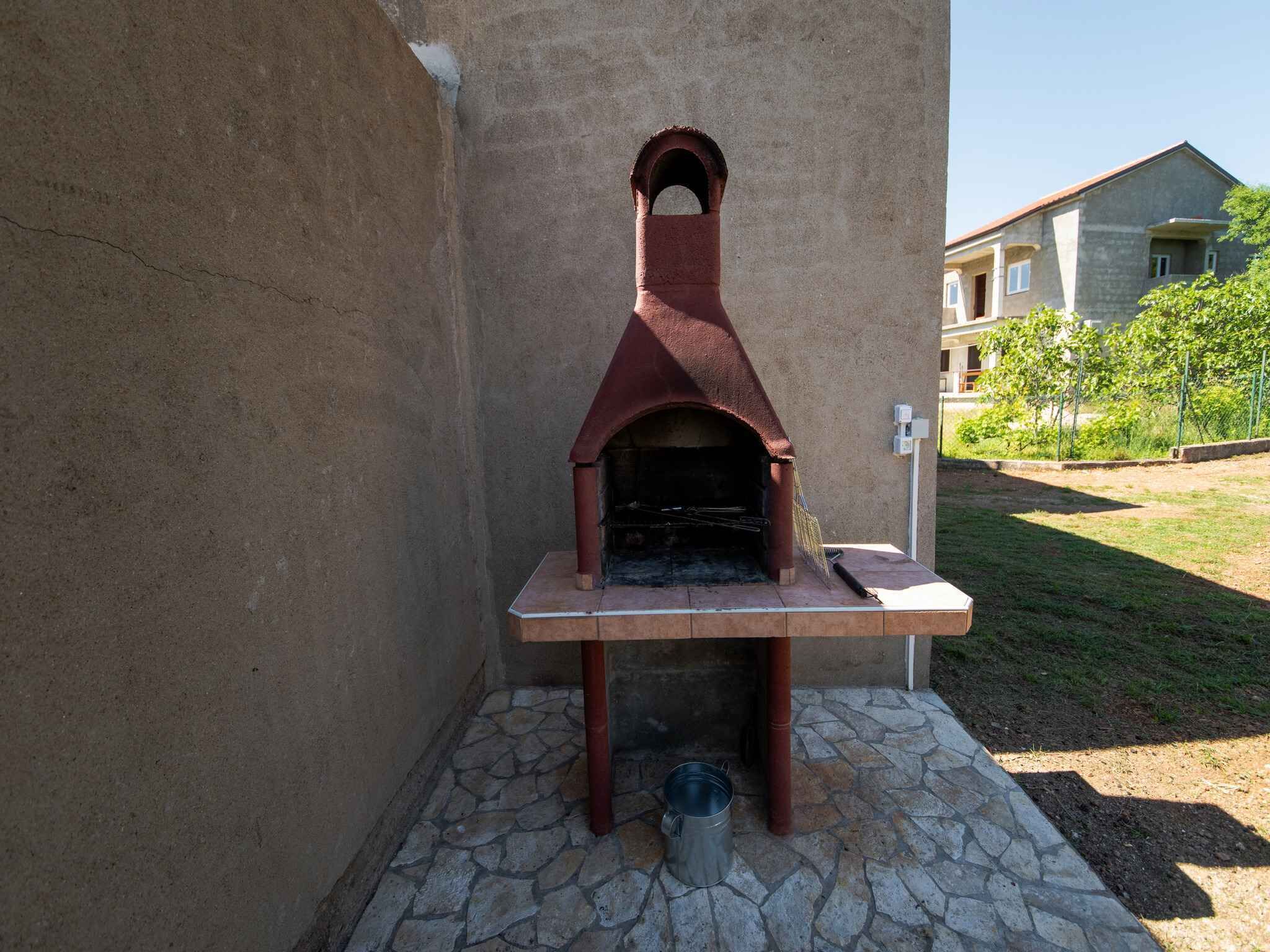 An outdoor brick oven with a stone base and a metal bucket nearby.