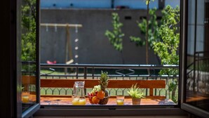 Una mesa con frutero, jarra y vasos en un balcón con vistas a un edificio y árboles.