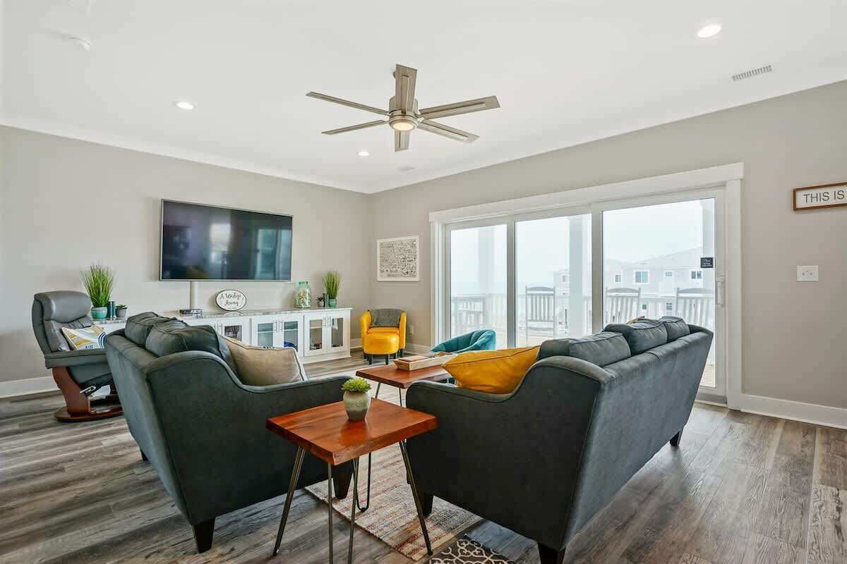 A modern living room with a flat-screen TV, two sofas, a ceiling fan, and a large window with a view.