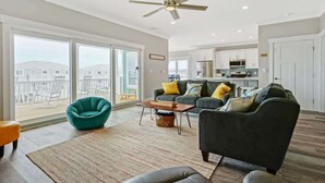 A spacious living area with a large window, a ceiling fan, and a view of a balcony. - A Wedge Away by Brunswick Vacation Rentals: Near Beach, Great Views, Heated Pool (Ocean Isle Beach)