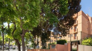A tree-lined street with modern apartment buildings, a gated entrance, and a clear sky. - Rincon Dorado by Interhome (Torremolinos)