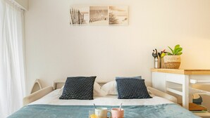 Una cama bien hecha con una bandeja de desayuno, que incluye zumo de naranja y bollería, en una habitación de decoración sencilla y vistas a la playa.