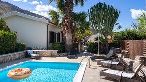 Un área de piscina con sillones de descanso, una palmera y un cactus.