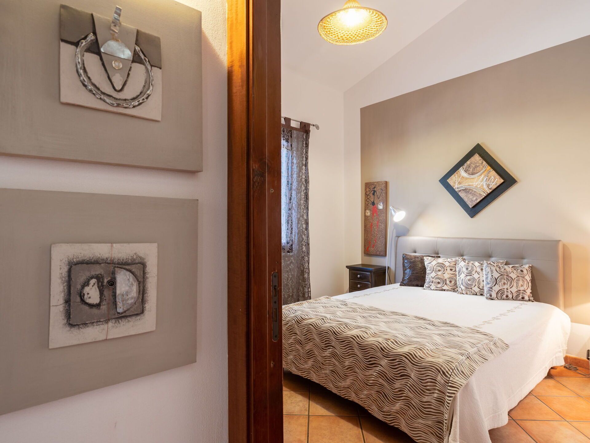 Une chambre à coucher avec un lit, une table de chevet, une lampe et des œuvres d’art accrochées aux murs.