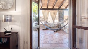 Una puerta abierta que da a un patio con una hamaca, un ordenador portátil sobre un escritorio y un muro de piedra.