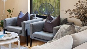A modern living room with grey sofas, a round table, and a large window with bamboo view. - Jacaranda Lane | Sleek & Modern | Central (Margaret River)