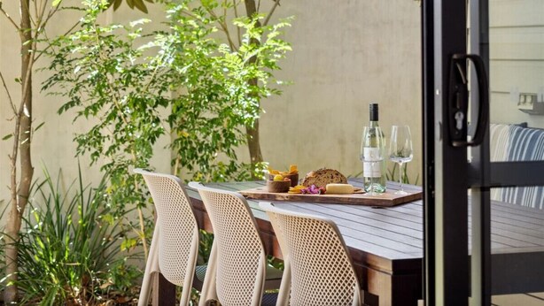 An outdoor dining area with wicker chairs and a wooden table set with food and wine glasses. - Jacaranda Lane | Sleek & Modern | Central (Margaret River)