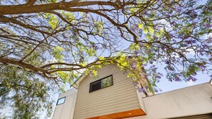 A modern building with a garage door, a small window, and a tree with purple flowers. - Jacaranda Lane | Sleek & Modern | Central (Margaret River)