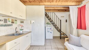 A kitchen with white cabinets, a wooden countertop, and a tiled floor. There is a staircase leading to a bedroom with a white sofa and a red curtain. -  Kipi Village Zakynthos (Ζάκυνθος)