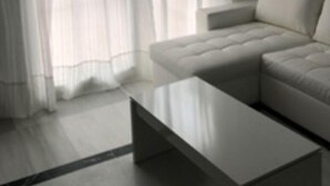 Un salon moderne avec un canapé d’angle, une table basse et des rideaux légers.
