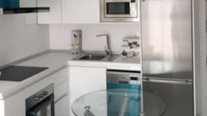 Une cuisine moderne avec des armoires blanches, un réfrigérateur en acier inoxydable, un four à micro-ondes, un lave-vaisselle et un îlot central avec un plan de travail en verre.